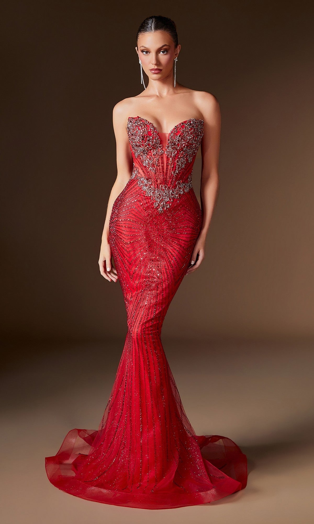A woman wears the Ladivine KV1129 Strapless Long Mermaid Prom Gown—a bold red, beaded bodycon evening dress—showcasing intricate embellishments and a dramatic silhouette against a plain brown background.